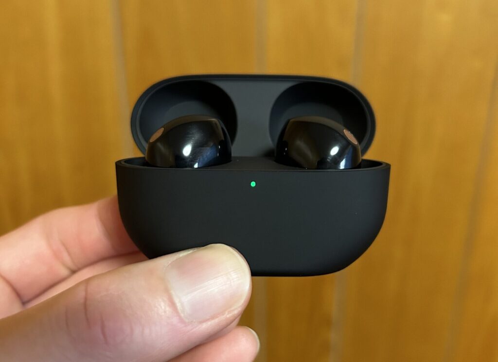 WF-1000XM5 を充電ケースに収納した状態で、LED が点灯している実写写真。高級感とコンパクトさを表現。