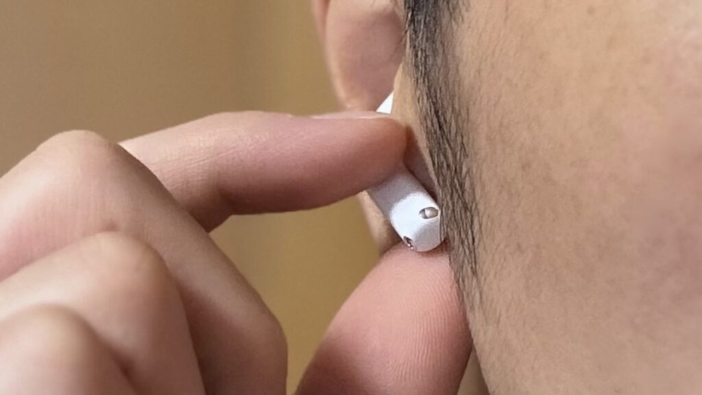 AirPods 5のステムを指でなぞって音量を調整している様子（音量スワイプ操作）