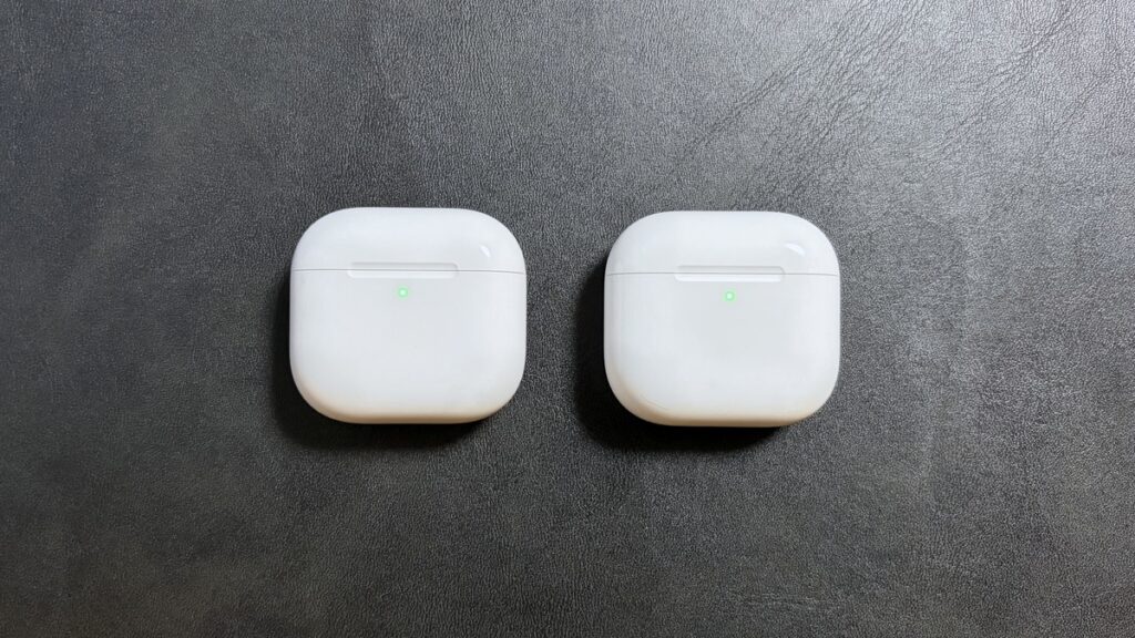 AirPods 5（左）とAirPods 4（右）の充電ケース正面比較（ランプ点灯時）。ランプが表面に浮かび上がるデザインは共通